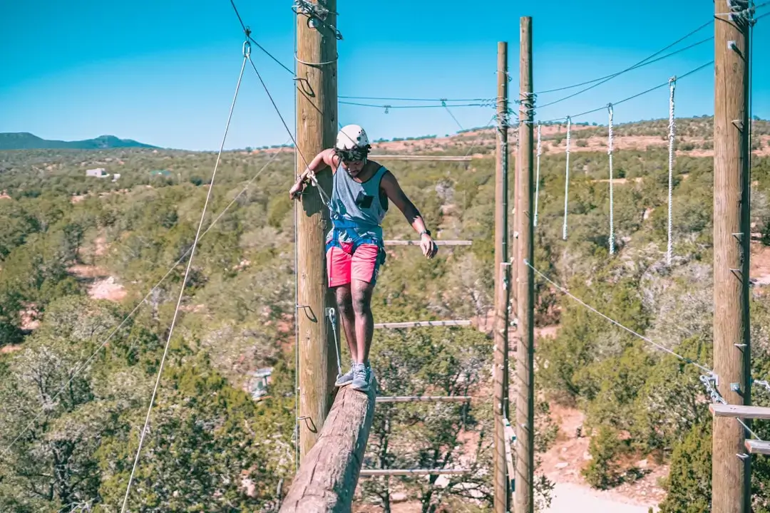 A person navigating a challenging wooden bridge and ropes course high in the trees at an outdoor adventure park.