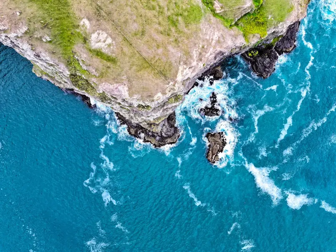 An aerial bird's-eye view of the dramatic turquoise waves crashing against the rugged limestone cliffs of the Portuguese coastline.