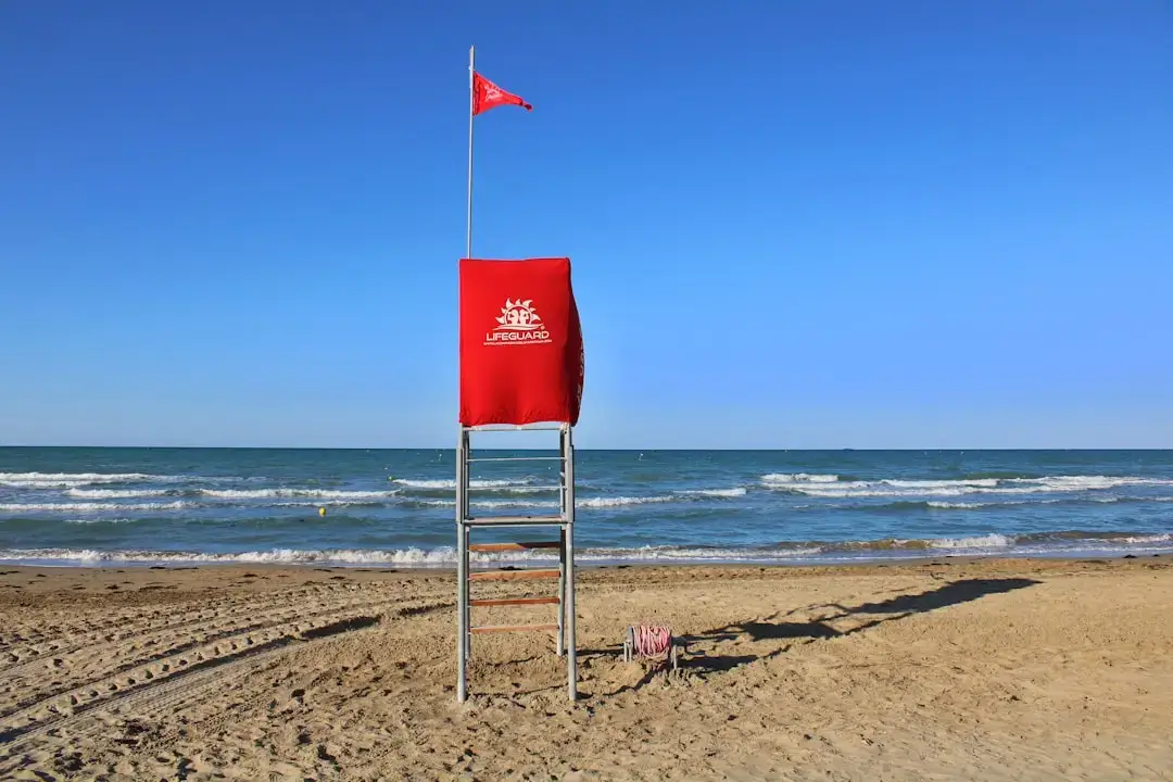 A vibrant red warning flag blowing in the wind on a sandy beach to signal swimming safety conditions