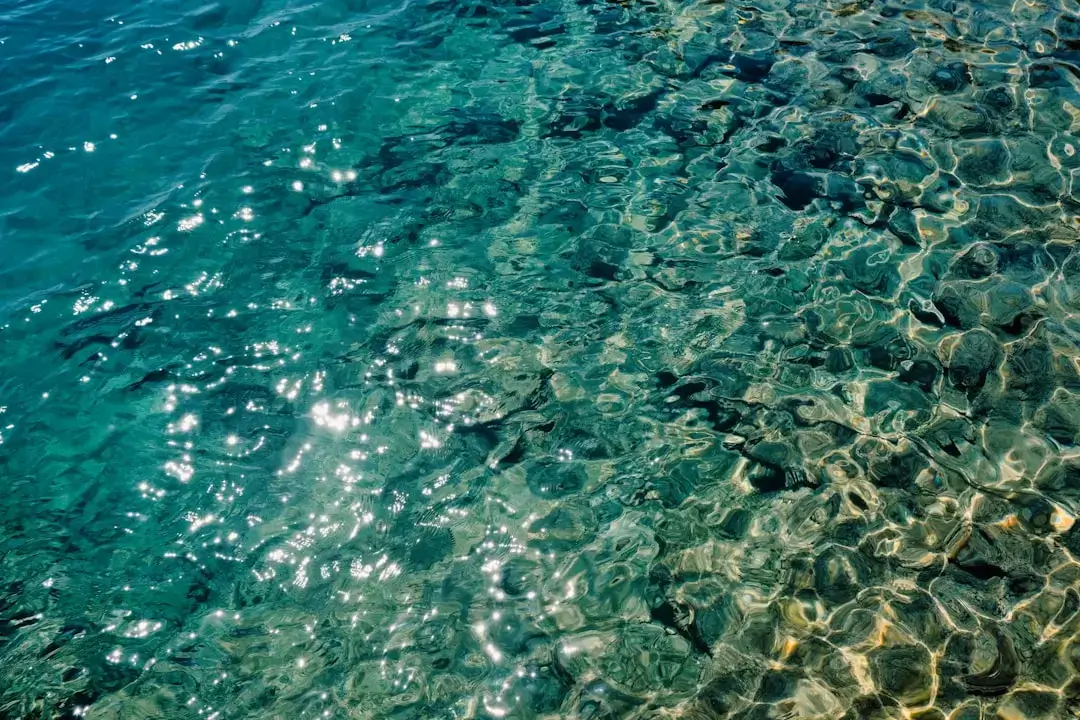 Top down view of crystal clear turquoise ocean water with sunlight reflecting on the sandy bottom