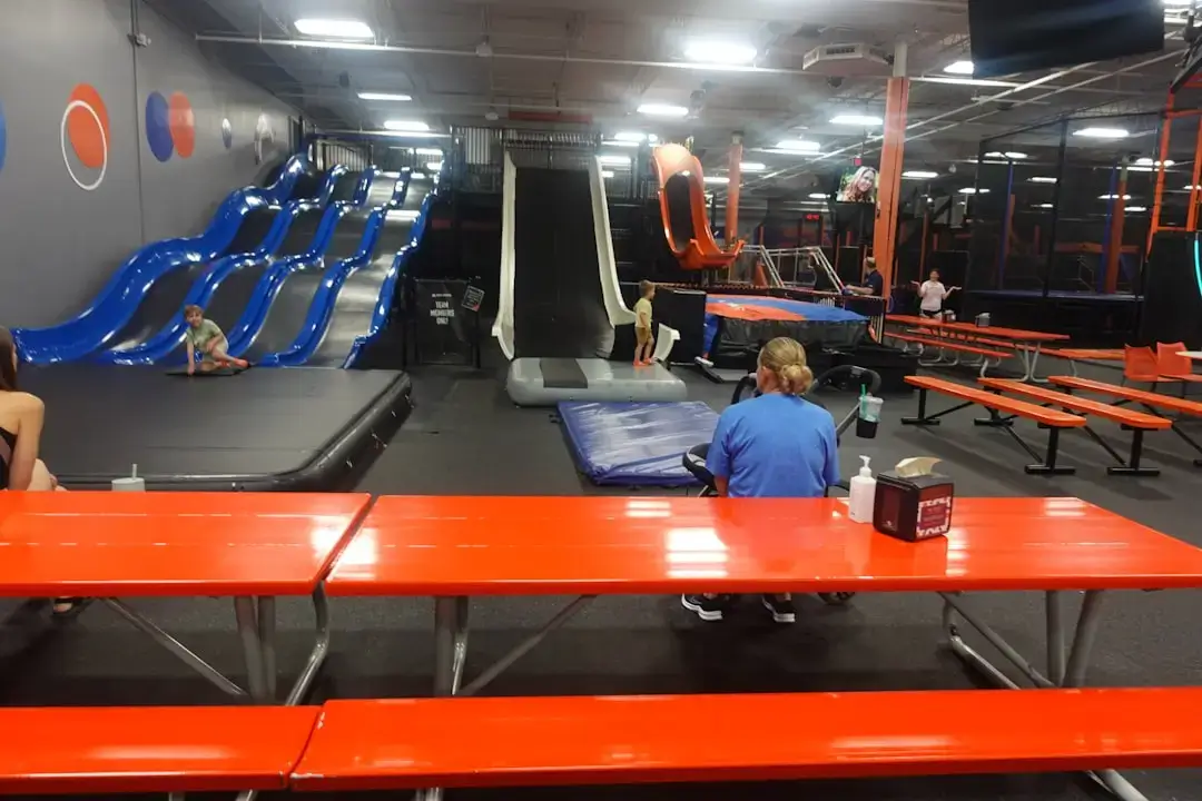 A group of energetic children playing on colorful climbing structures and obstacles inside a modern indoor adventure park.