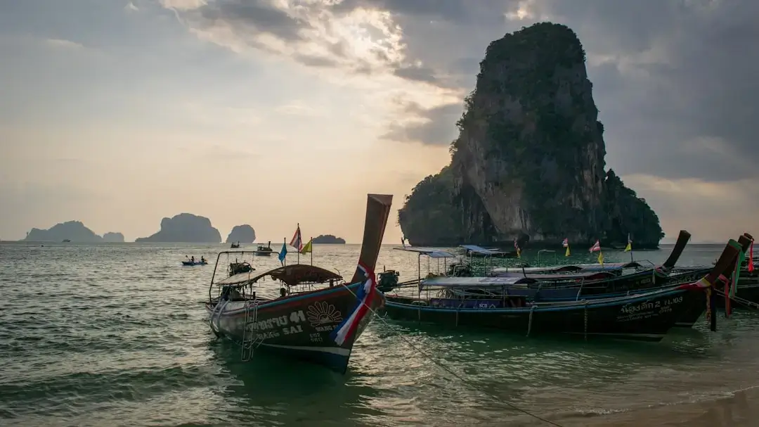 A traditional wooden longtail boat anchored on a white sand beach with turquoise water in Krabi, Thailand.