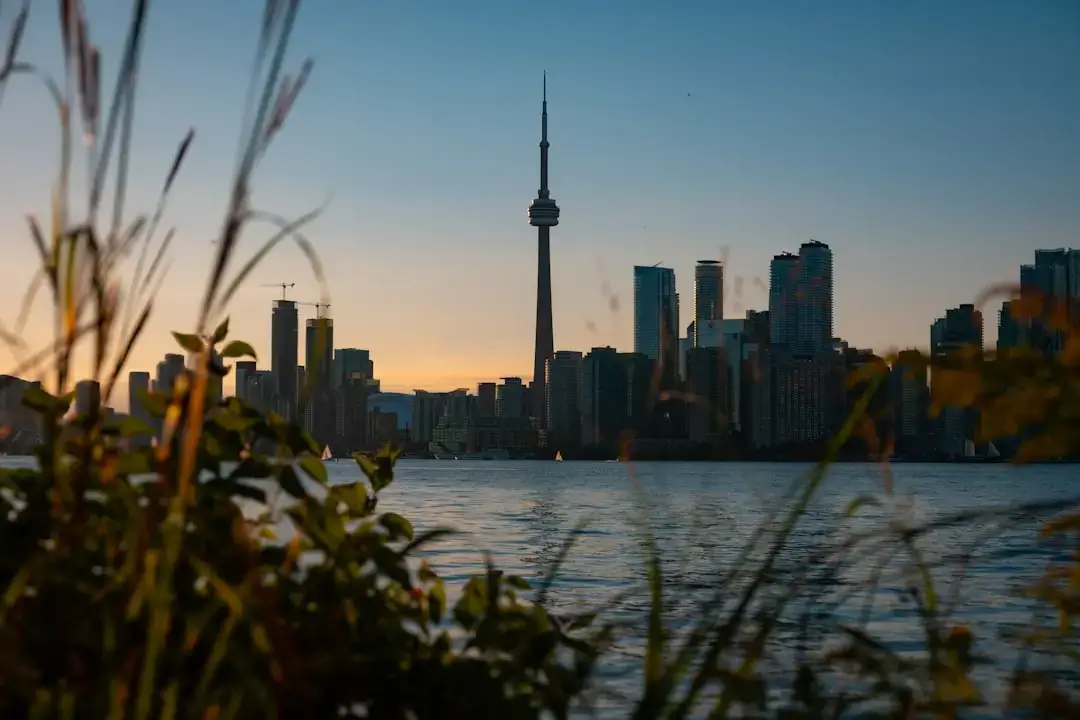 A panoramic view of the modern Toronto city skyline featuring the CN Tower and tall glass skyscrapers against a bright sky.