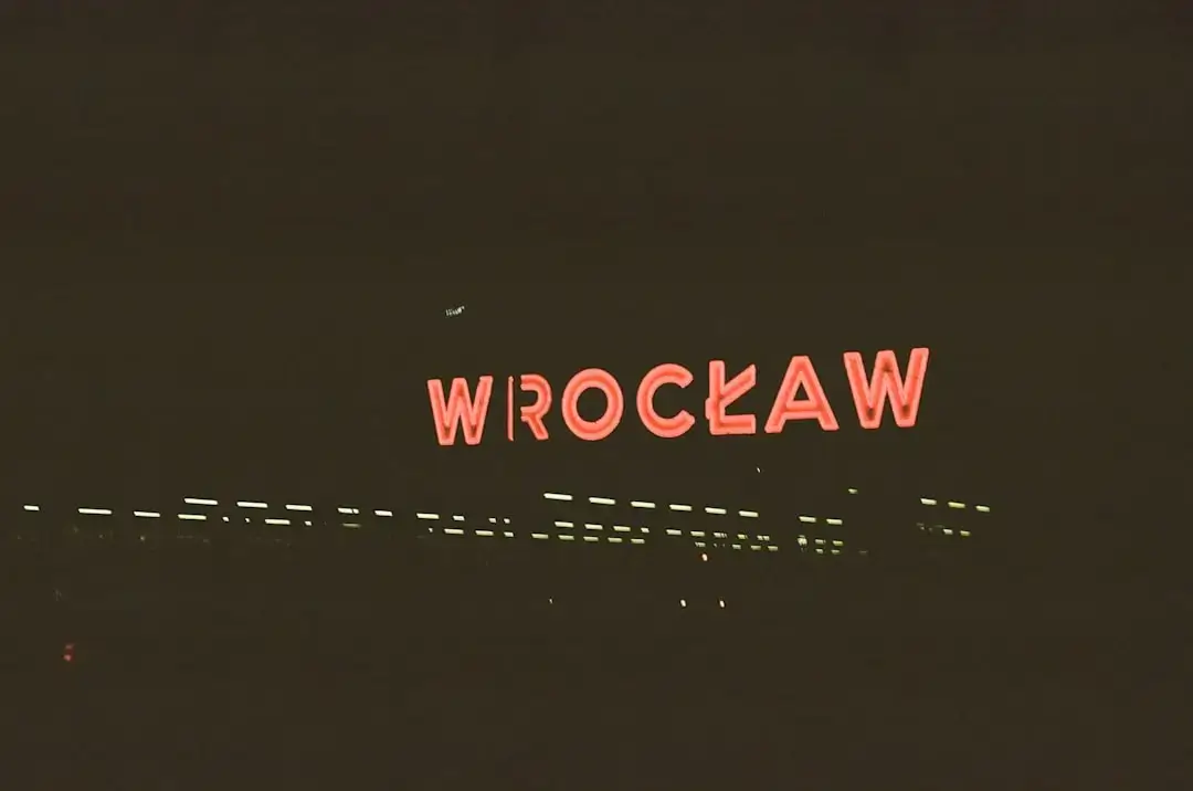 A vibrant alleyway in Wroclaw featuring a collection of glowing vintage-style modern neon signs against the night sky.