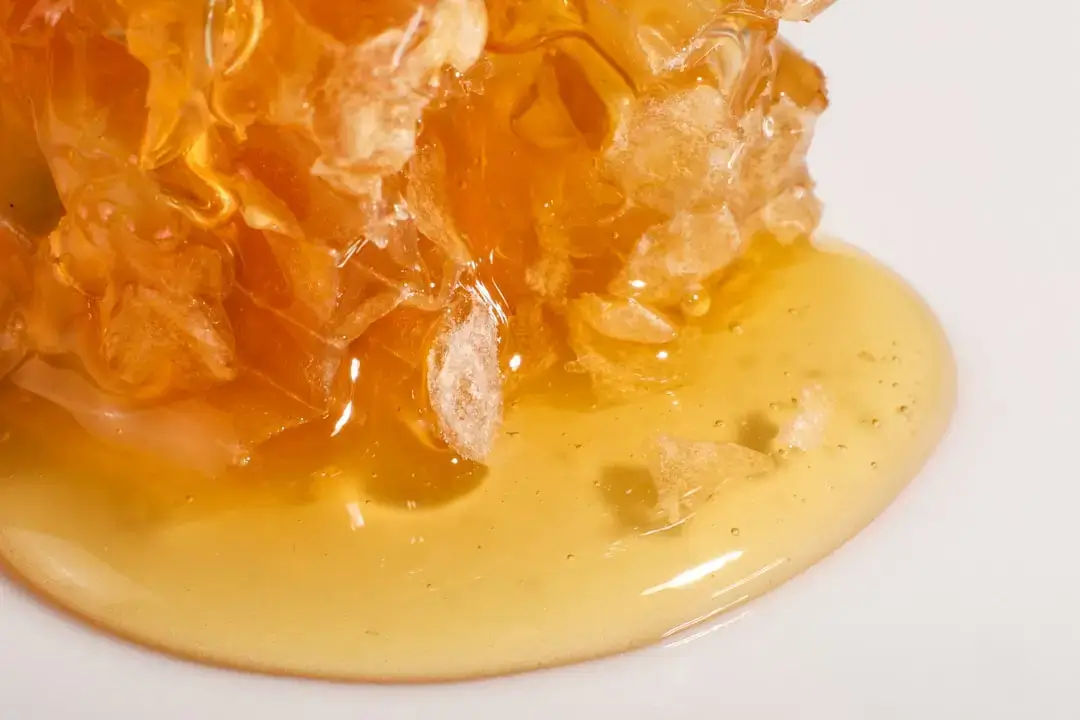A clear glass jar filled with golden organic honey with a wooden dipper on a rustic background.