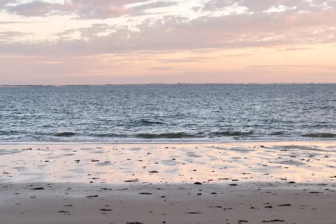 Two empty wooden lounge chairs facing a calm ocean during a vibrant orange and purple sunset.