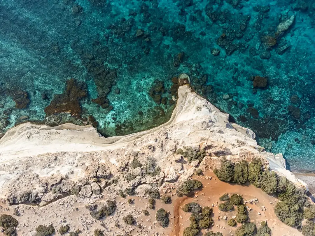 A white rental car parked on a scenic coastal road overlooking the Mediterranean sea in Cyprus during a sunny day.