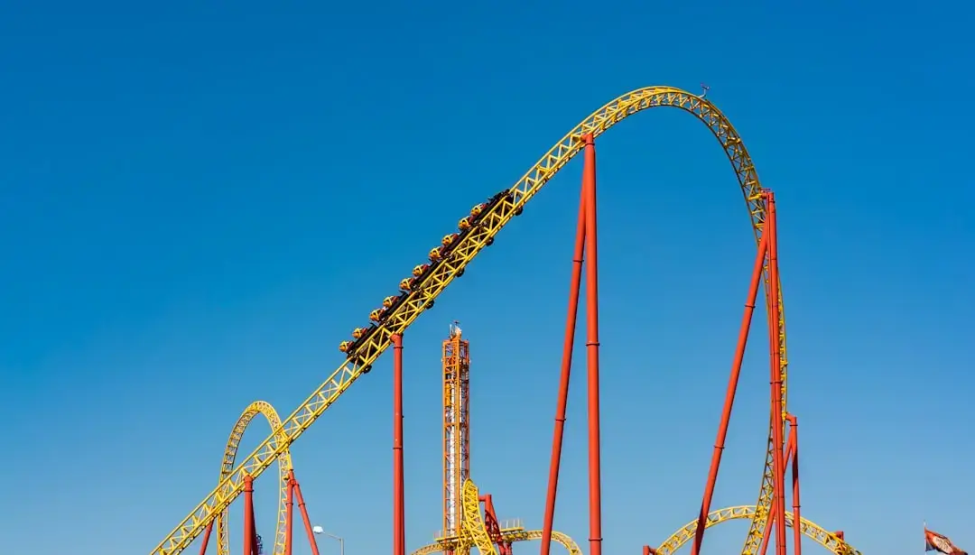 A dramatic silhouette of a winding roller coaster track against a vibrant orange and purple sunset sky at a theme park.