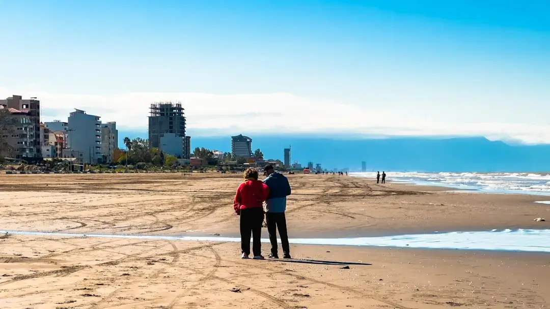 An active senior couple walking hand in hand along a sandy beach shoreline at sunset.