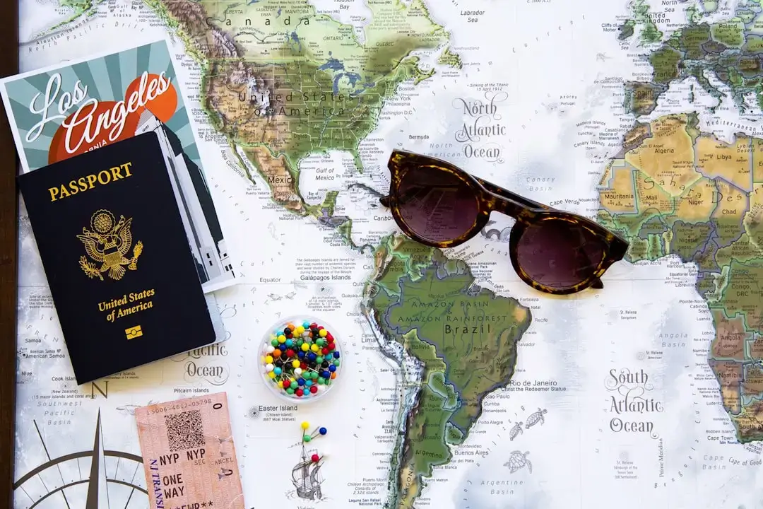 An aesthetic flatlay of travel planning essentials including a map, passport, camera, and notebook on a wooden surface