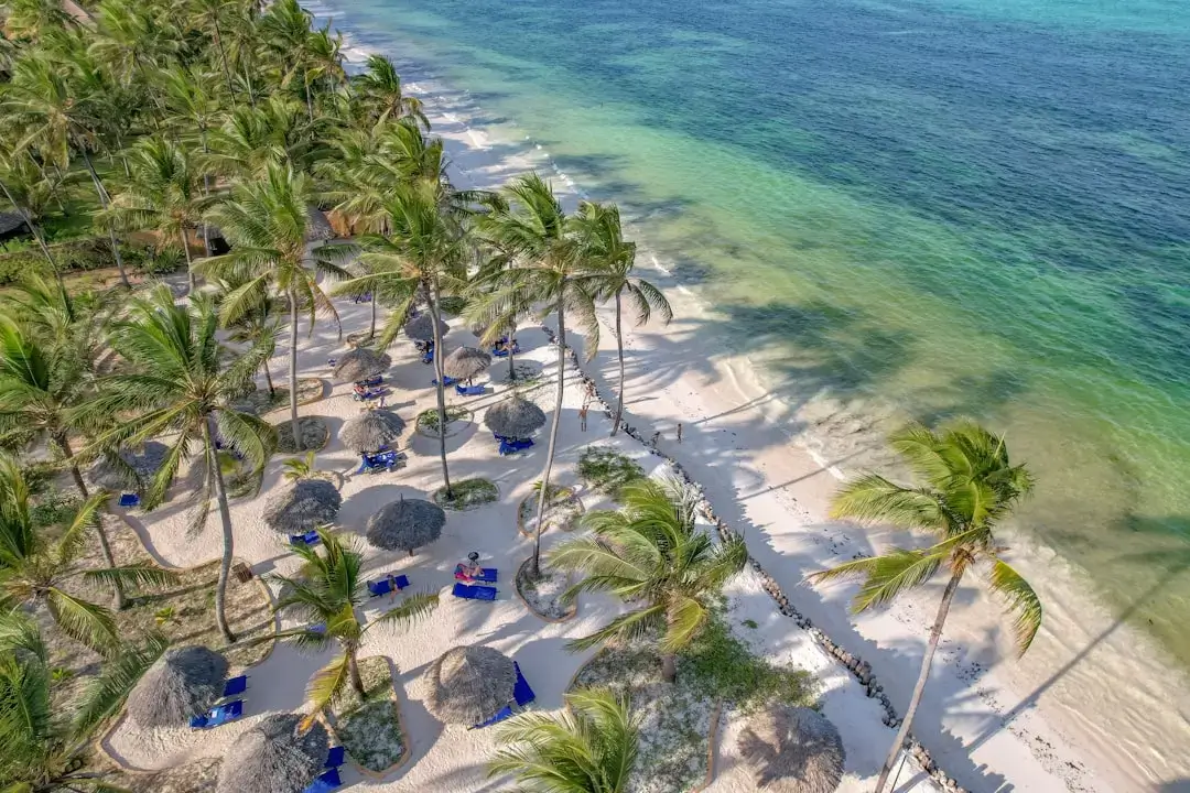 Crystal clear turquoise waters and white sand at a tropical beach in Zanzibar with wooden boats and palm trees.