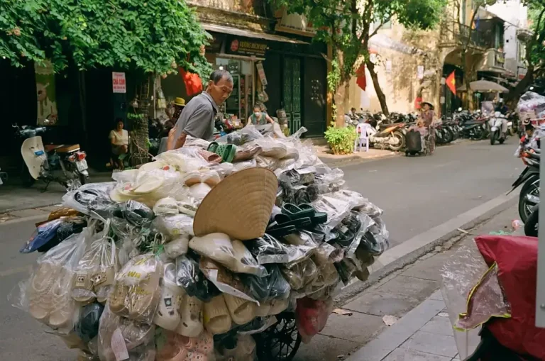 A man pushing a cart full of items down a street