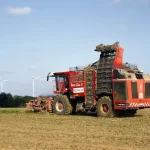 Red harvesting machine in a field with wind turbines.
