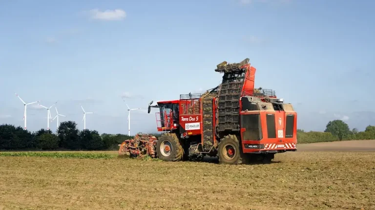 Red harvesting machine in a field with wind turbines.