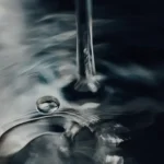Close-up of hands turning off a sleek bathroom faucet to conserve water and prevent waste.
