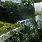 Modern train traveling through lush indoor jungle with waterfall.