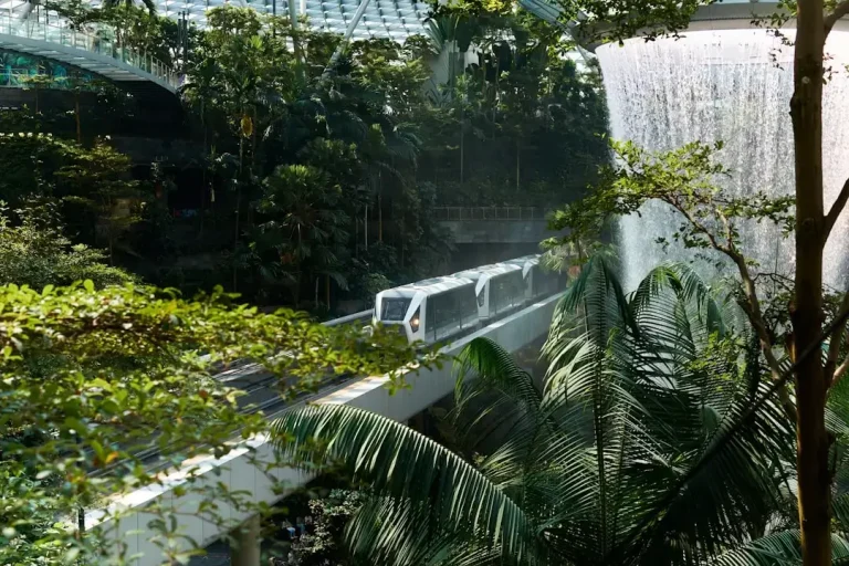 Modern train traveling through lush indoor jungle with waterfall.