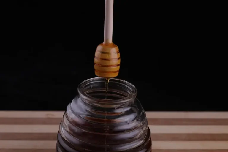 A close up of natural golden honey dripping from a wooden dipper, illustrating how to identify real honey.