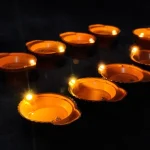 Several small tealight candles burning in aluminum cups on a rustic table representing household waste before disposal