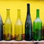 A close-up of empty green glass bottles sitting outdoors, representing recycling and waste management.