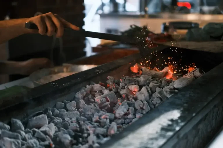 A person safely cleaning black soot and ash from a fireplace for proper waste disposal.