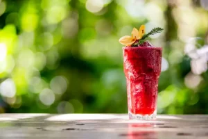 A refreshing tropical drink on a wooden table overlooking a luxury resort swimming pool, representing an all-inclusive plus vacation package.