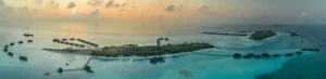 Aerial view of a tropical turquoise lagoon and white sand islands in the Maldives under a bright sky.