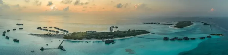 Aerial view of a tropical turquoise lagoon and white sand islands in the Maldives under a bright sky.