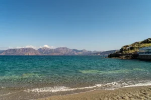 Crystal clear blue waters of the Mediterranean Sea hitting the rocky coast of Crete under a bright sun.