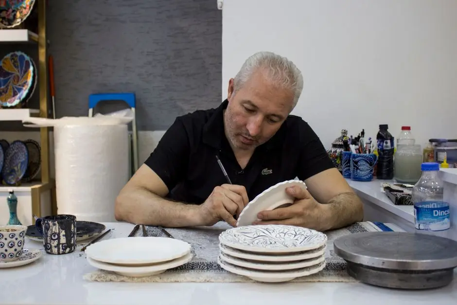 Mężczyzna w pracowni maluje ręcznie skomplikowane wzory na ceramicznych talerzach.